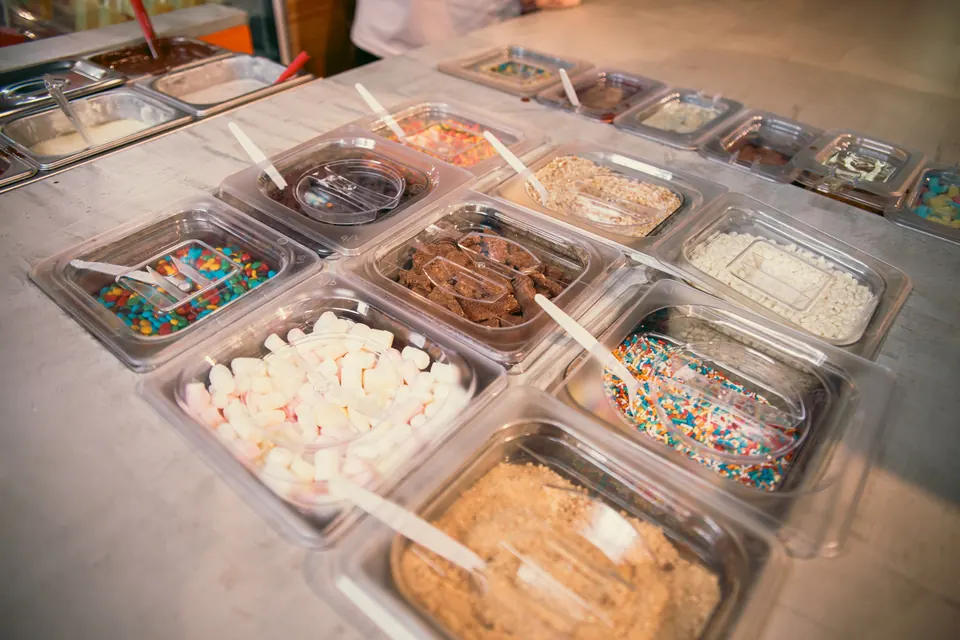 Barra de toppings de IKE con masmelos, chispas, galleta y salsas para armar paletas en vivo