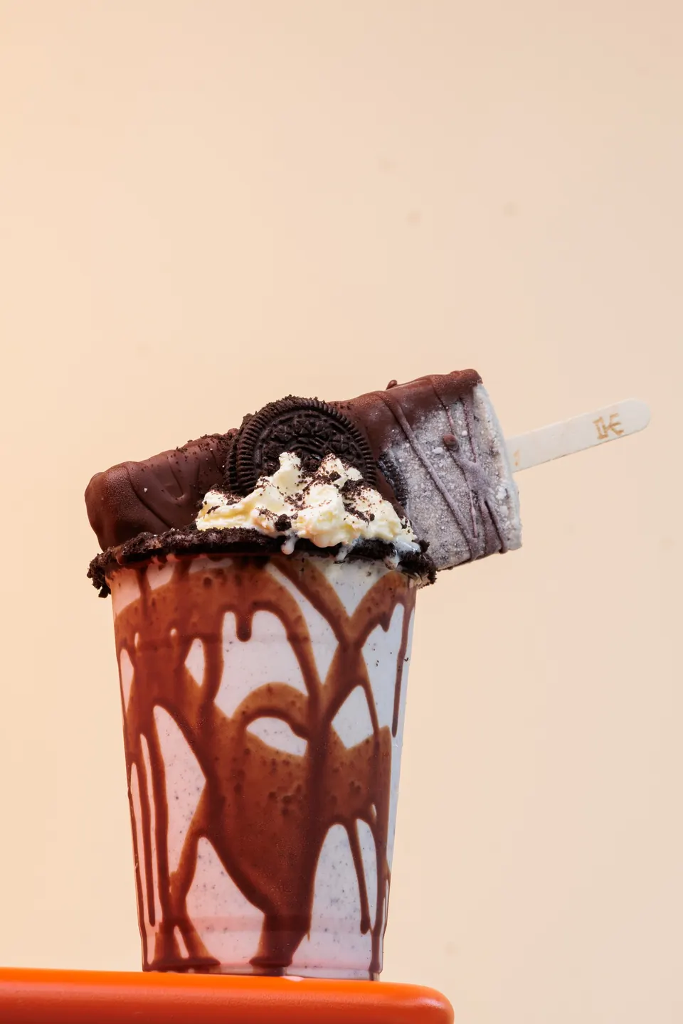 Malteada IKE de chocolate con paleta y galleta encima sobre una mesa naranja