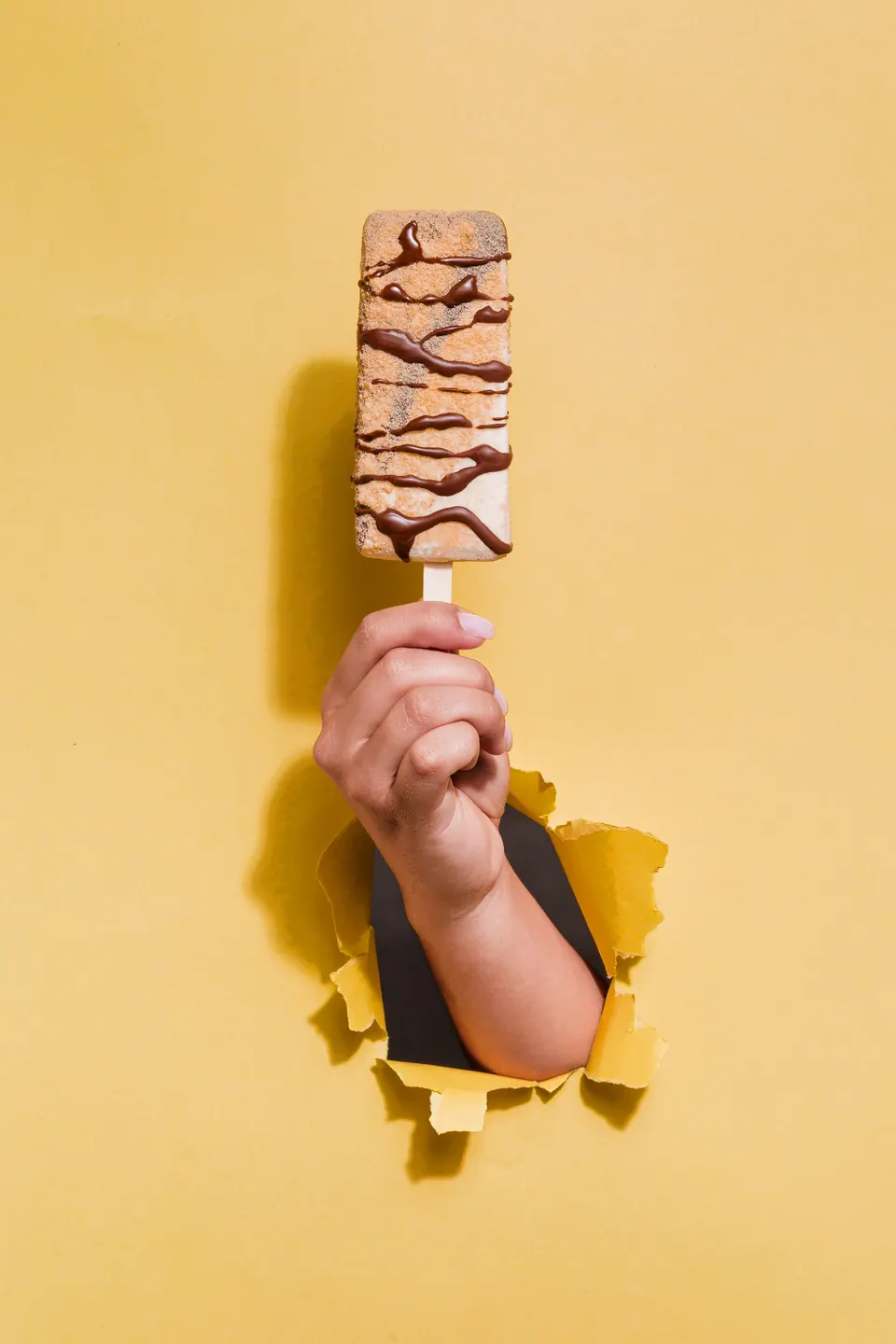 Paleta cremosa IKE nivel La Atrevida con baño y rayas de chocolate, sobre fondo amarillo